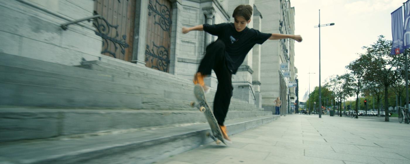 Boy on skateboard performing a trick near steps on a city street.
