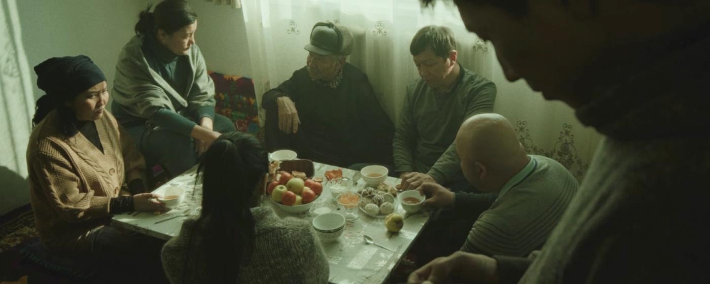 A family gathered around a table in a dimly lit room; solemn, tension-filled people.