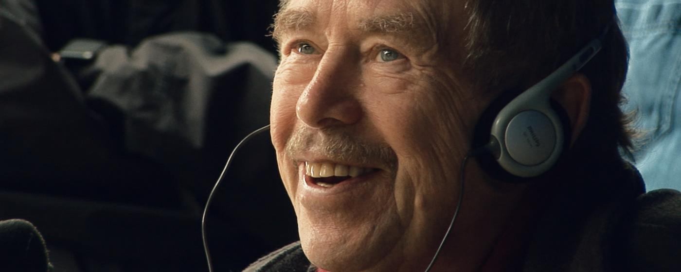 Václav Havel se sluchátky na uších se usmívá a hovoří s někým. 