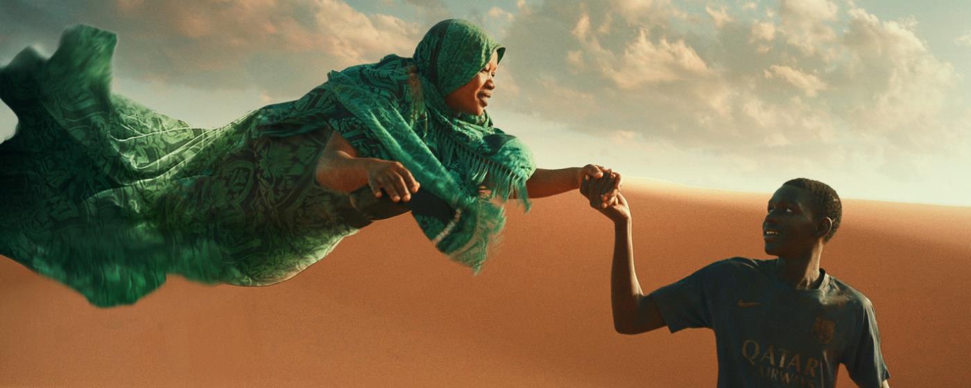 Woman in green floating above desert, holding hands with a guiding, smiling boy.