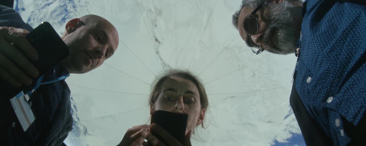 Three people looking down at a smartphone, viewed from below against a earth globe background.