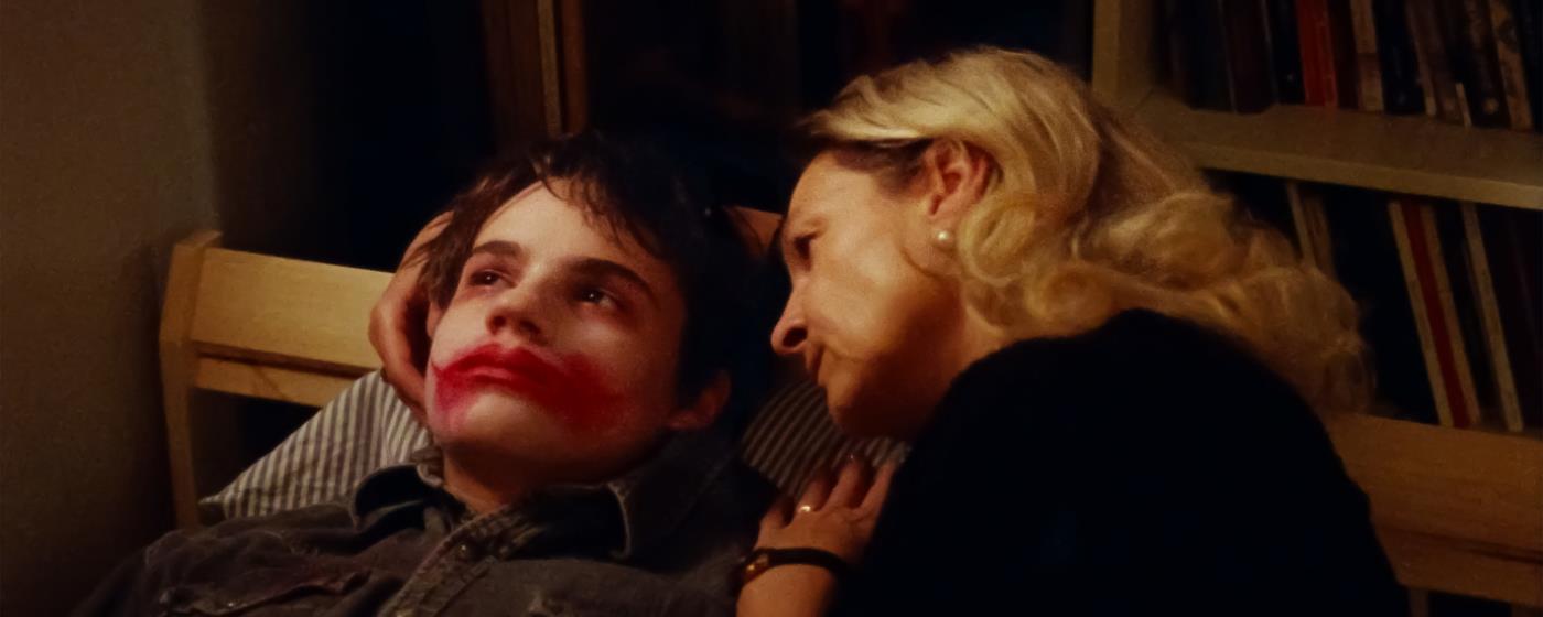 Žena objímá chlapce se smutným výrazem a červeným makeupem na ústech.