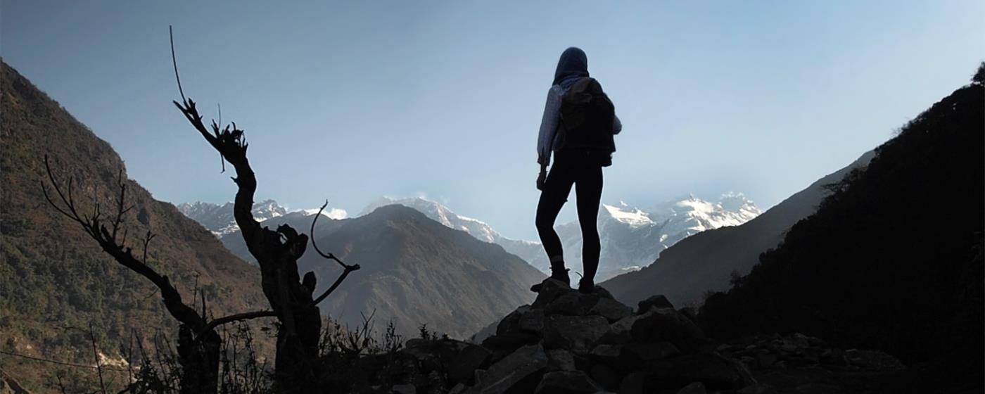 Female hiker silhouetted against mountains and sky.