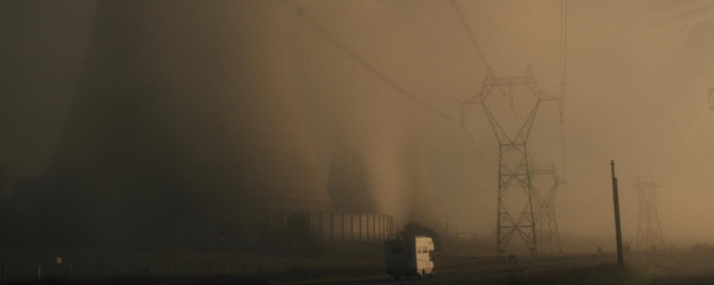 Power lines and electricity towers shrouded in mist with a truck on the road.