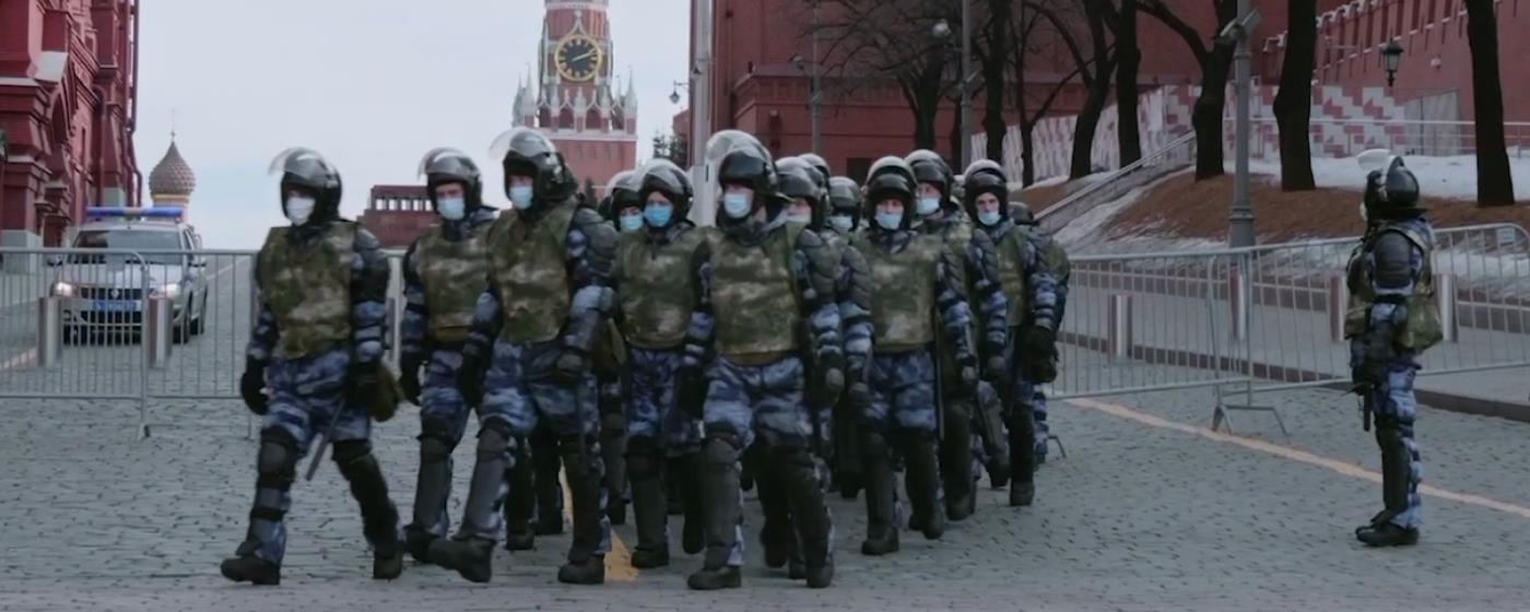 Skupina ozbrojených vojáků v maskovacích uniformách a s helmami kráčí po ulici.