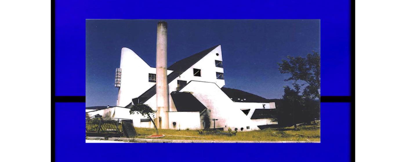 A white, uniquely-shaped building with a tall chimney against a blue background.