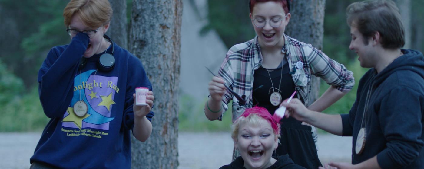 Čtyři mladí lidé se smějí venku, jednomu barví vlasy růžově.