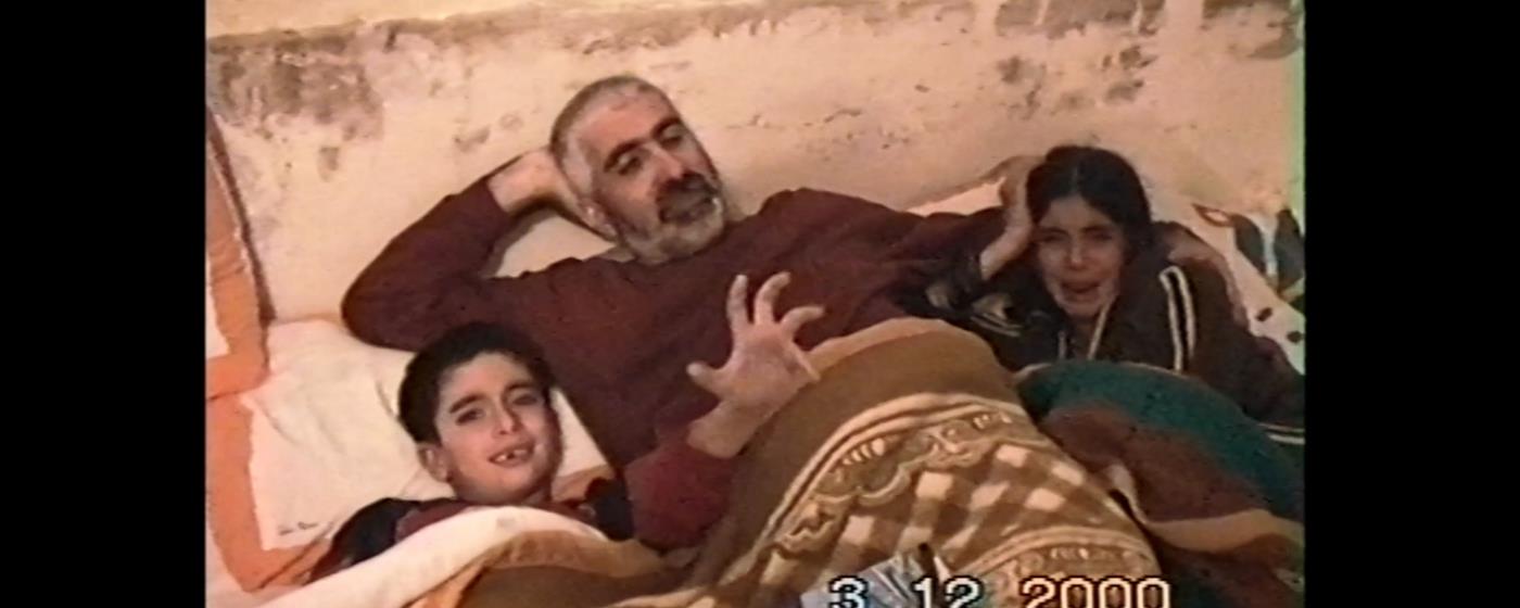 Muž a dvě děti relaxují, usmívají se na pohovce s dekou.