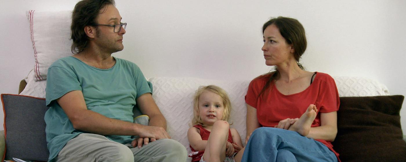 Concerned man and woman sitting on couch with a young child between them.