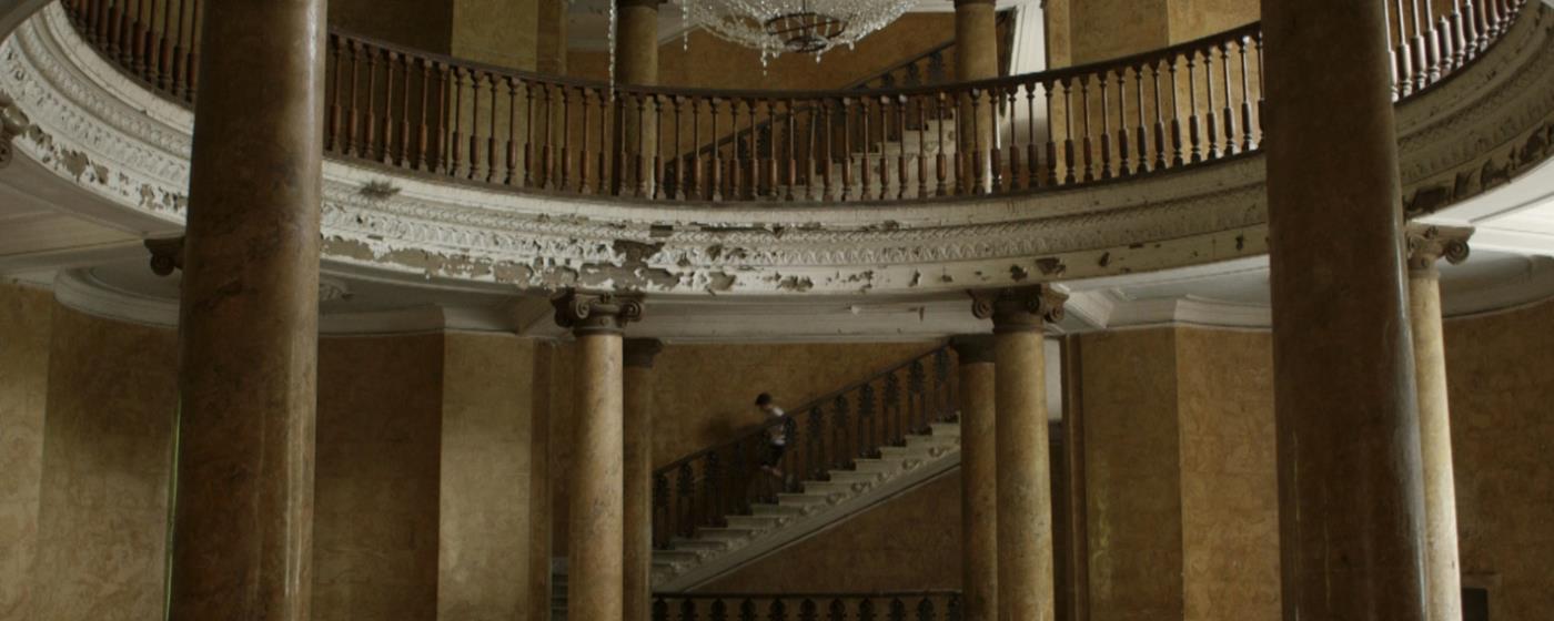Elegant, dilapidated room with columns, balcony, and staircase.