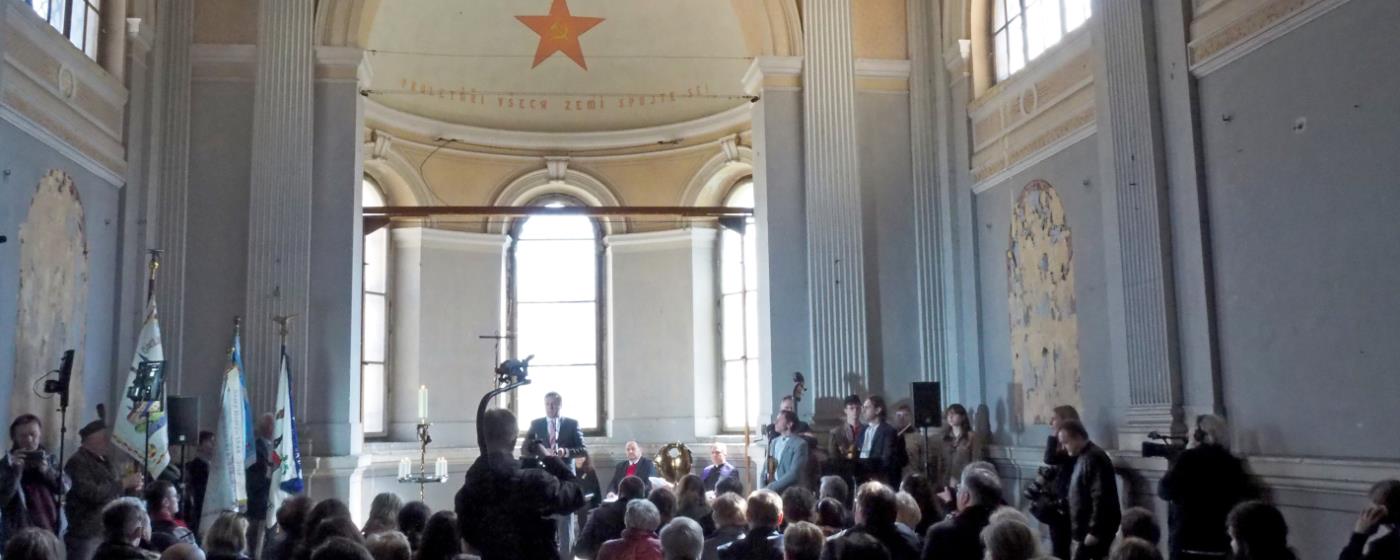 Interior of a grand room with people attending an event, featuring a large red star decoration.