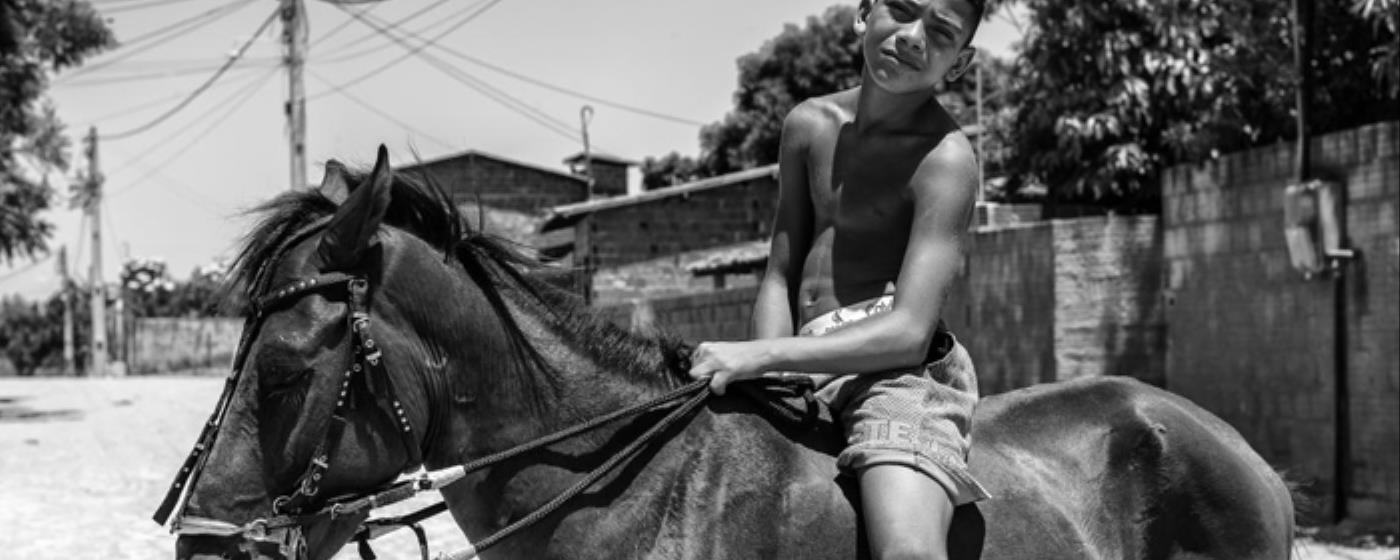 Chlapec sedí na koni a dívá se stranou na slunečné ulici.