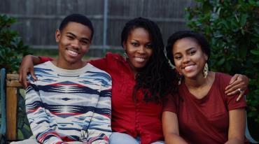 Family of three smiling on a bench outdoors.