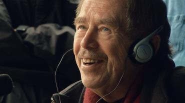Václav Havel se sluchátky na uších se usmívá a hovoří s někým. 