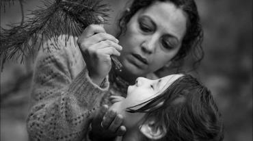 Woman feeding child water from a pine tree branch, monochrome image.