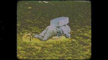 Person in gray outfit lying face down on grass with block on back.