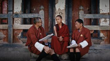 Two men and one boy in traditional robes sitting and talking by a building.