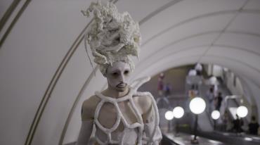 Person in avant-garde white costume and makeup in a subway station.