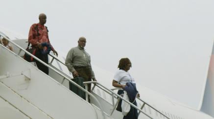 Four passengers descending airplane stairs on the tarmac.