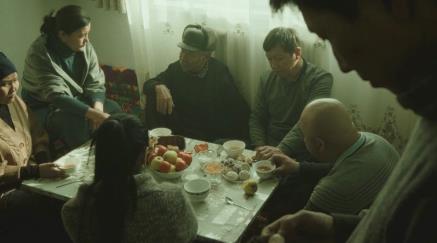 A family gathered around a table in a dimly lit room; solemn, tension-filled people.