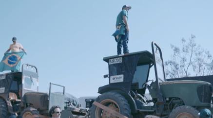 Dva muži stojí na střechách traktorů, jeden drží brazilskou vlajku.