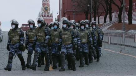 Skupina ozbrojených vojáků v maskovacích uniformách a s helmami kráčí po ulici.