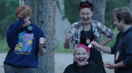 Čtyři mladí lidé se smějí venku, jednomu barví vlasy růžově.