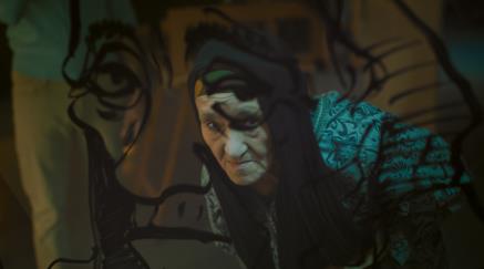 Person in costume with witch-like makeup in front of a mural of a woman traced. 