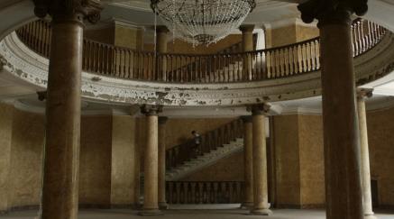 Elegant, dilapidated room with columns, balcony, and staircase.