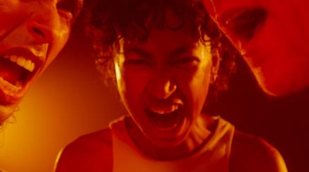 Three people yelling in a red-tinted light.