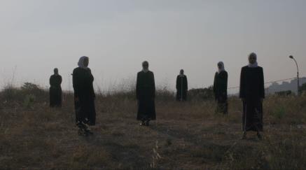 Several figures in dark robes, white headresses standing in a barren field.