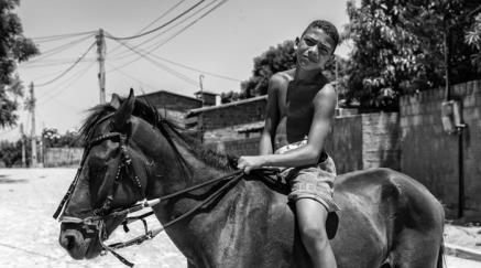 Young man riding a horse on a sunny street with buildings behind, monochromatic photo.